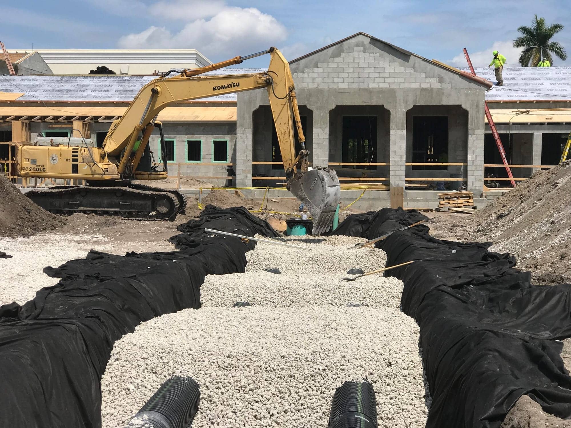Concrete block commercial building under construction with excavator and site drainage, Palm Beach County